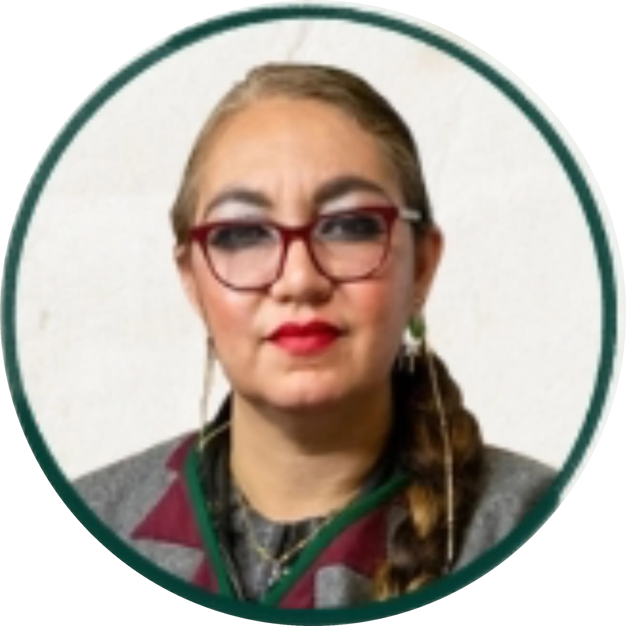 Portrait of a person with short blonde hair, burgundy-framed glasses, red lipstick, wearing a colorful striped shirt and green necklace