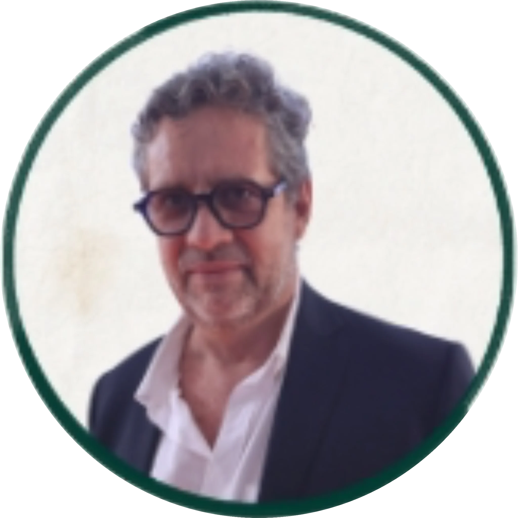Middle-aged man with gray hair and dark-framed glasses wearing a dark blazer and white shirt, circular portrait photo